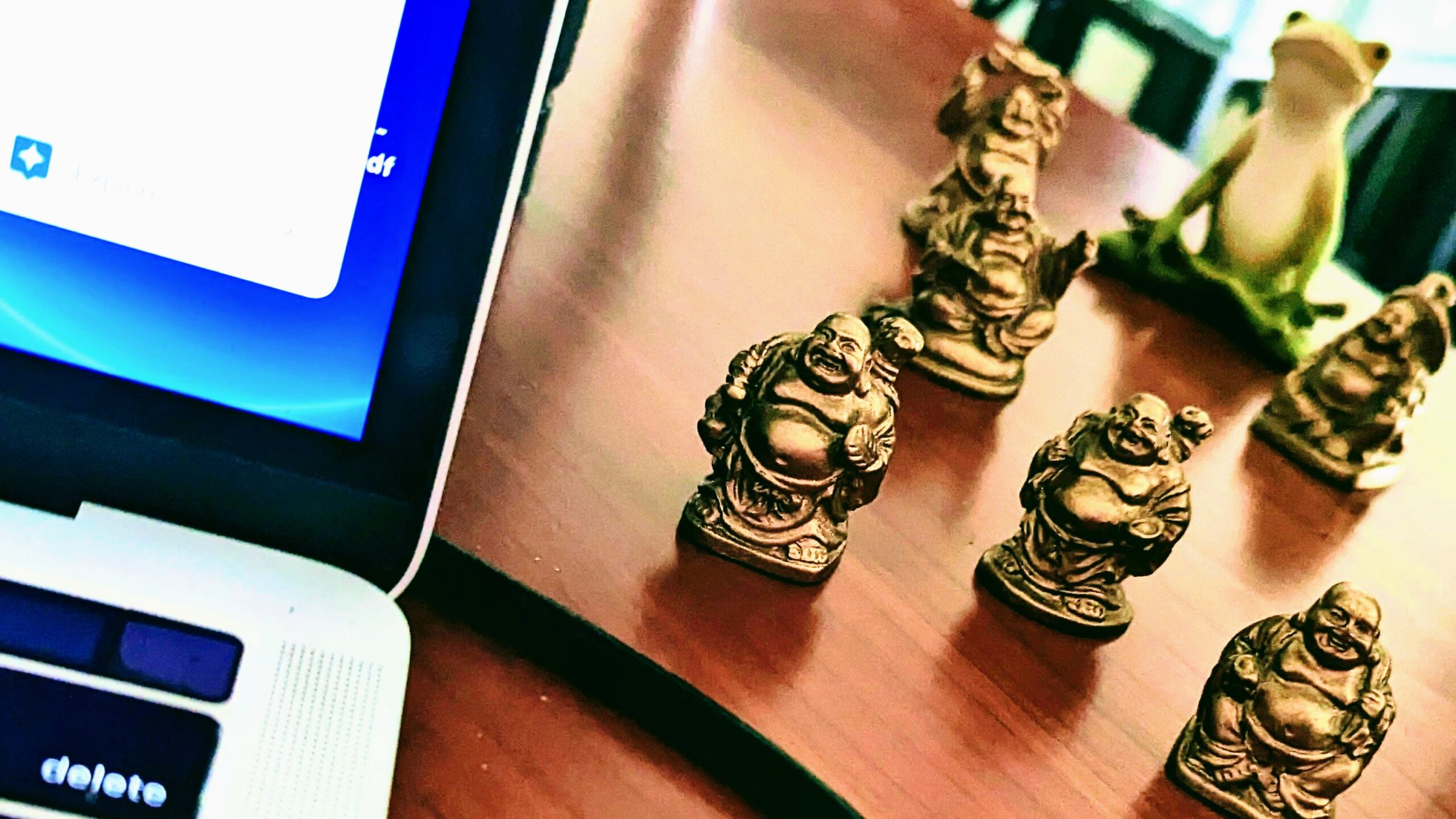 close up of little statuettes of laughing buddhas and a meditating frog perched beside a laptop on a desk