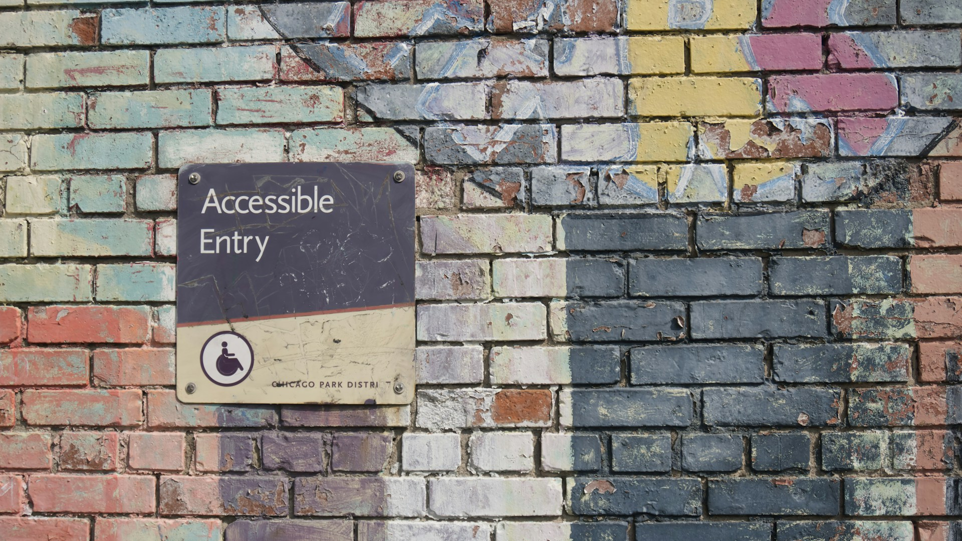 brick wall with faded paint, possible from a mural, with a sign reading "Accessible Entry" bolted into the bricks