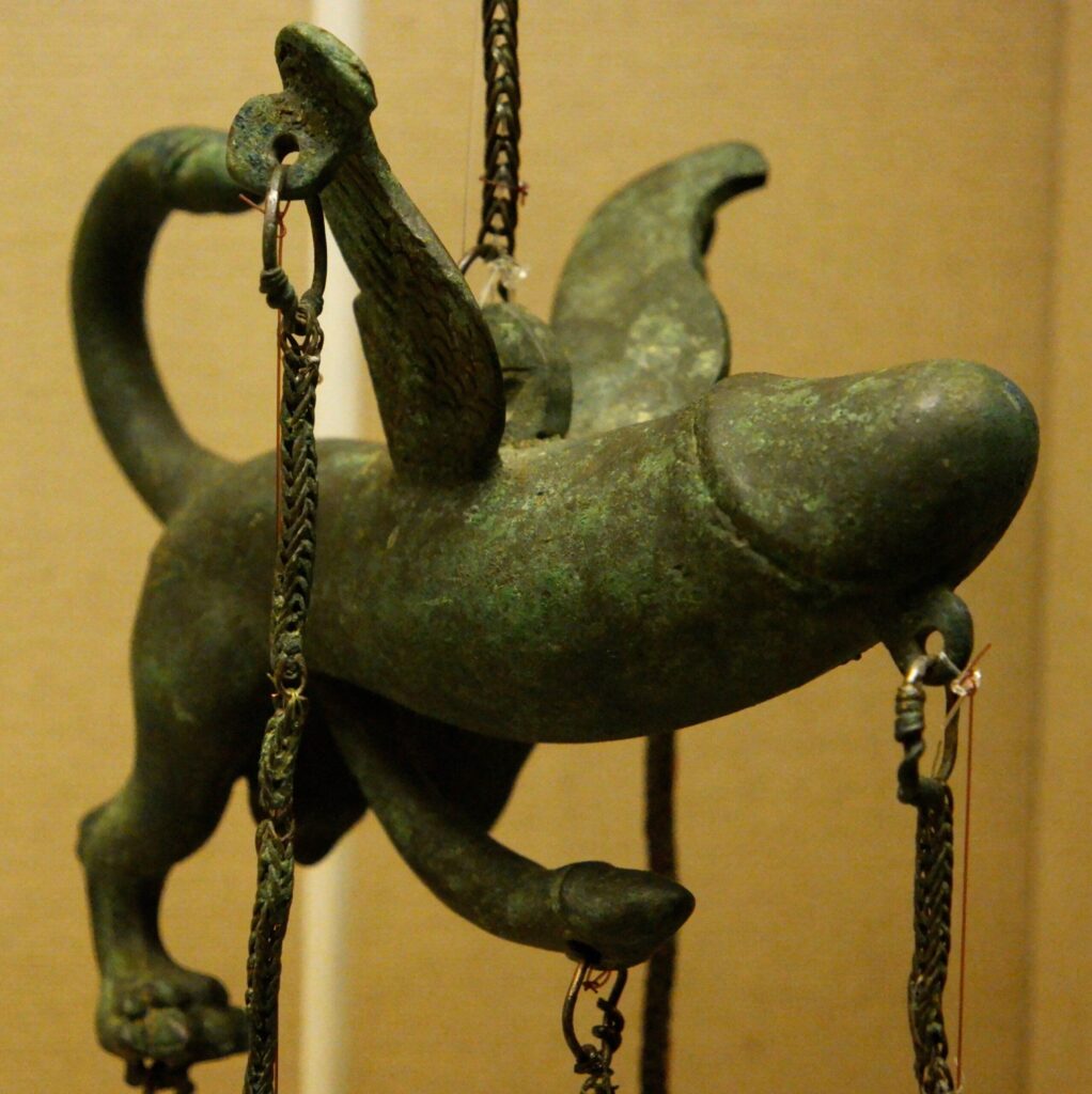 an ancient roman bronze charm in the shape of a winged phallus