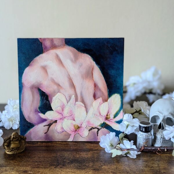 oil painting of a nude male torso against a dark blue background. it is displayed on a wooden table surrounded by flowers, a skull, and a little bottle of what might be called air freshener