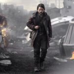 handsome man with determined expressions walks through smoldering wreckage